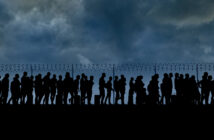 refugees and immigrants standing in front of a border fence