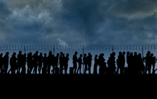 refugees and immigrants standing in front of a border fence